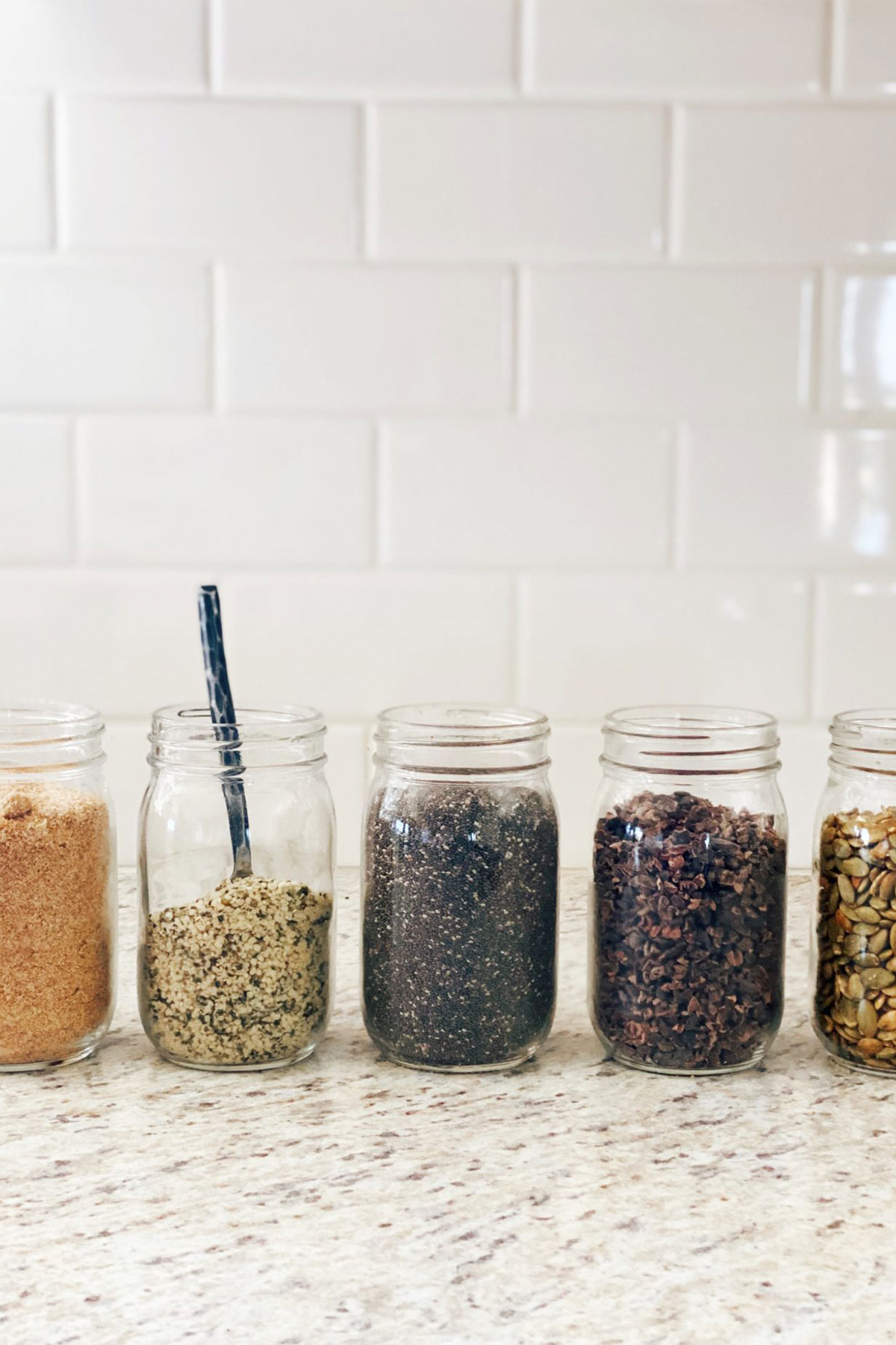 glass jars of flaxmeal, hemp hearts, chia seeds, cocao nibs, pumpkin seeds