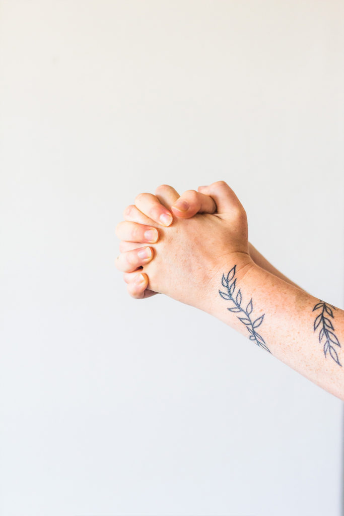 Hands praying with tattoo on arm