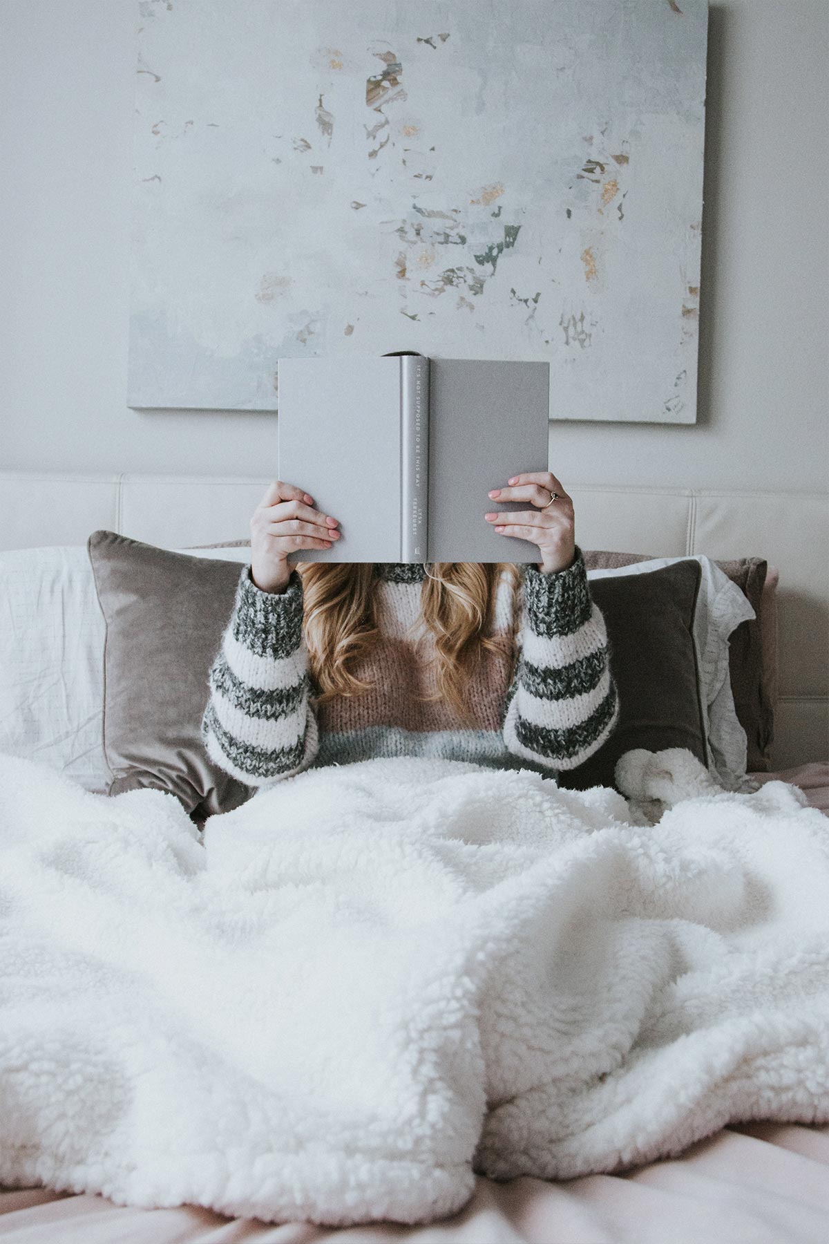 girl reading a book in bed with white sheets