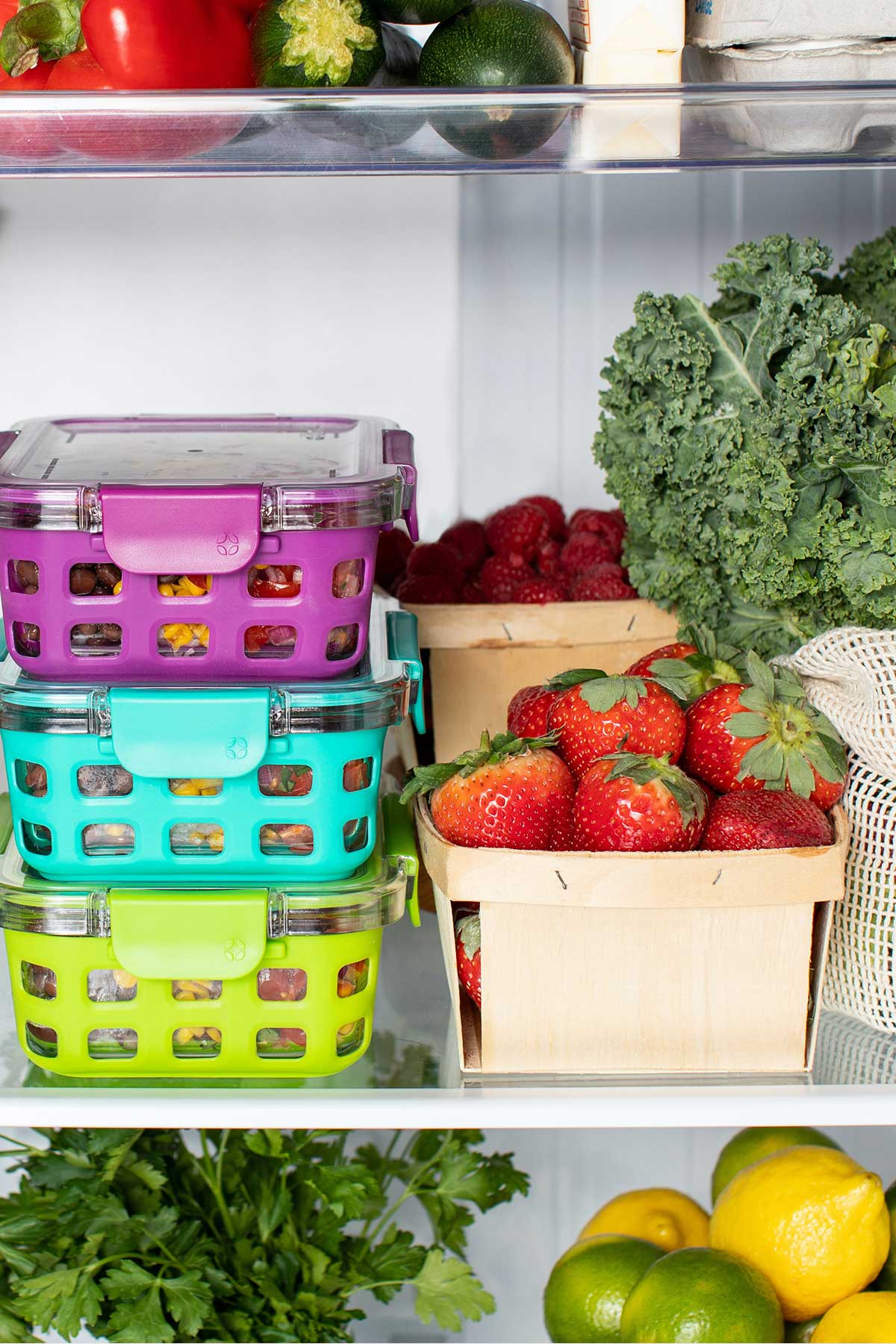 Refrigerator view with healthy containers of food, strawberries, kale, lemons, limes, cilantro, brussels sprouts, milk