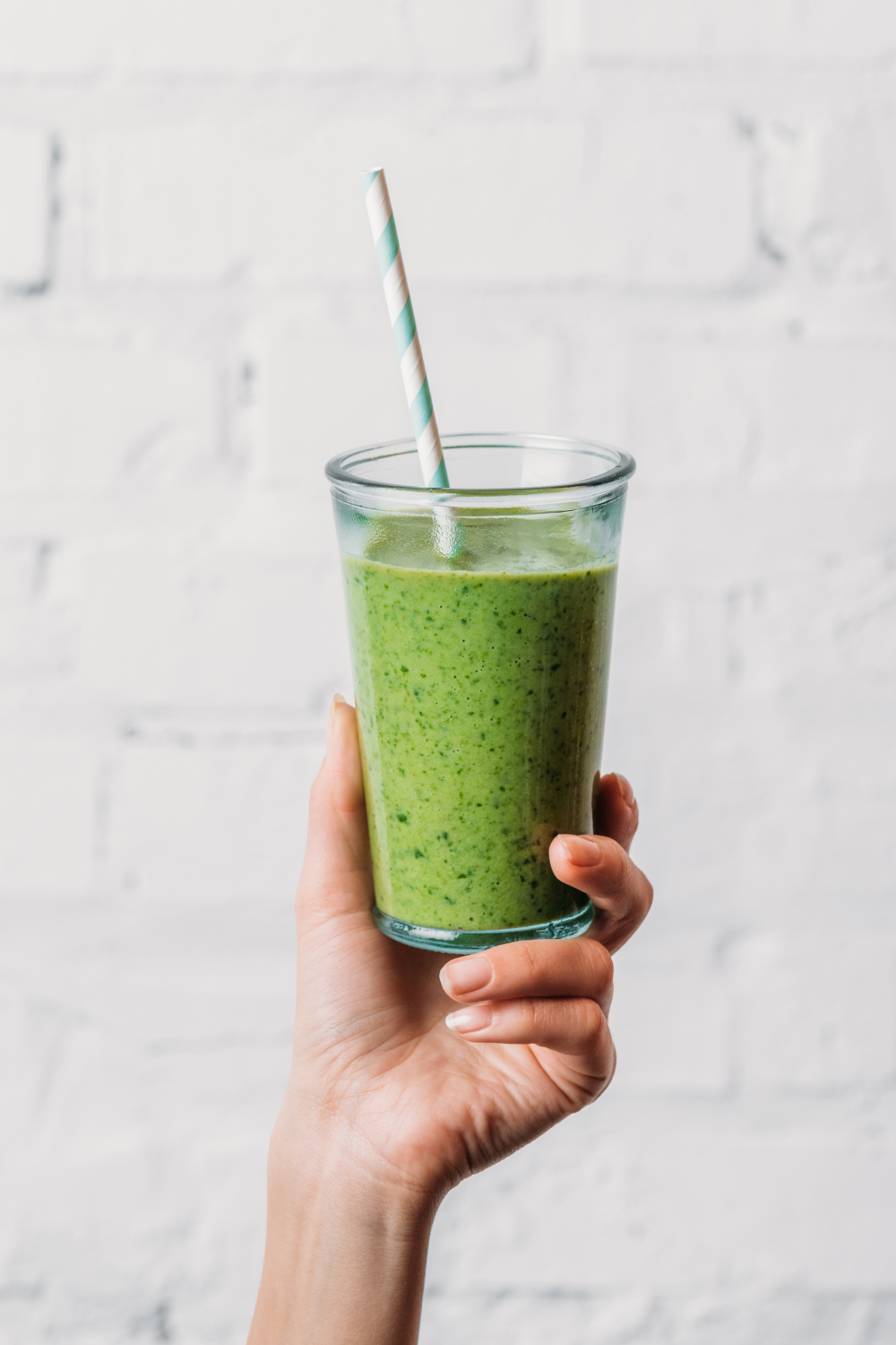 hand holding a green smoothie with a paper straw