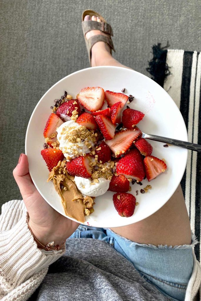 person holding a plate of strawberries and cream with granola and chia seeds